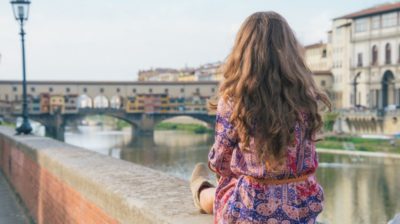 A young woman sitting on the Arno River looking at the Ponte Vecchio in Florence, Italy