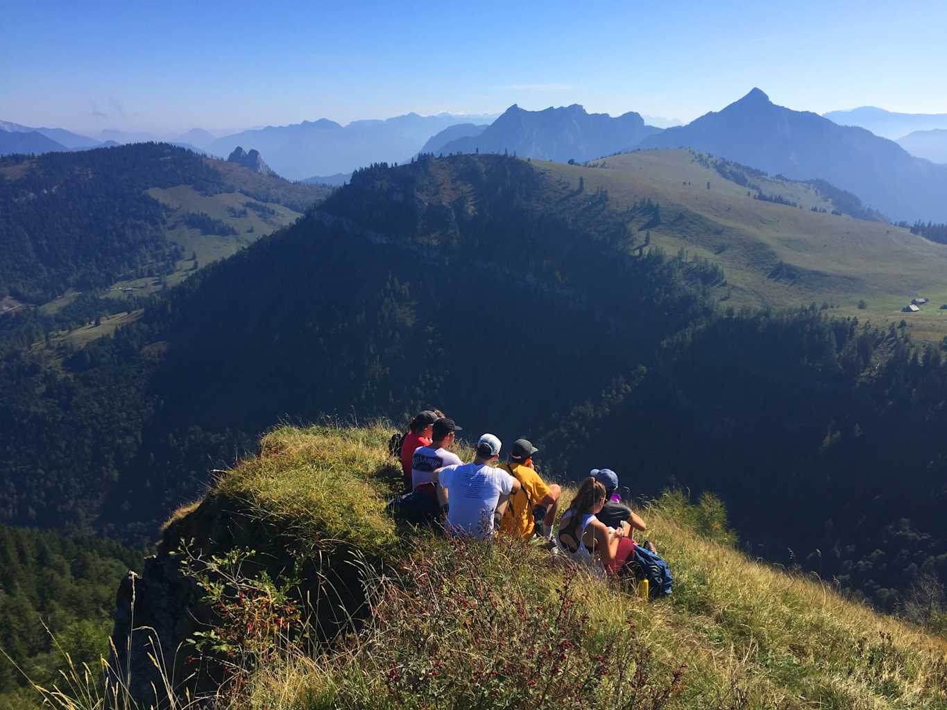 A group of student sitting on a grassy hill overlooking a view of mountains.