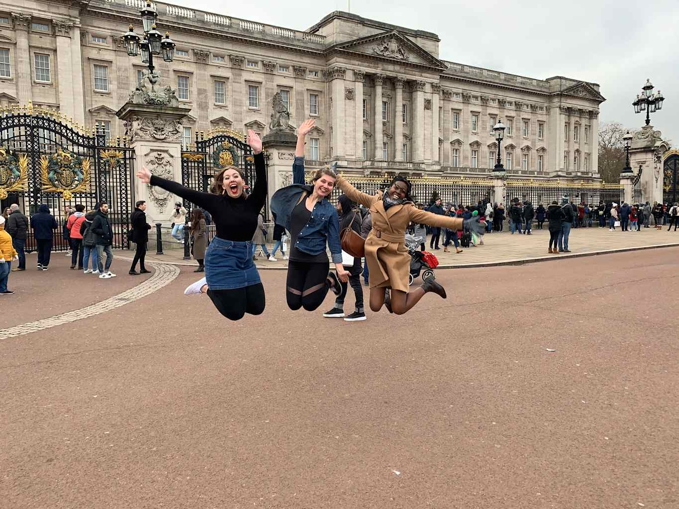 Three women jumping in the air in front of Buckingham Palace in London.