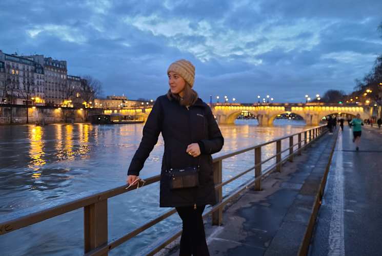A student standing near a river in Paris during the evening.