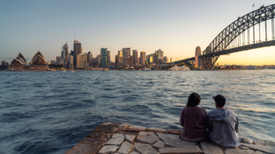 Two young people sitting beside the Sydney Harbor in Sydney, Australia